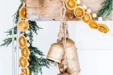 natural Christmas mantel decor with fir branches, dried citrus slices, large vintage bells and pompoms is gorgeous