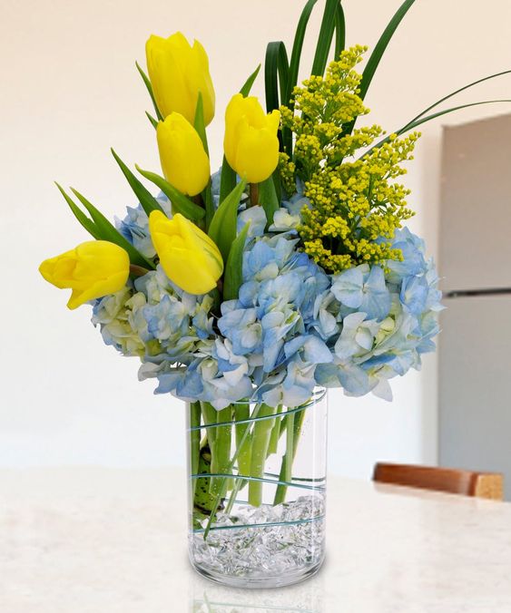 a bright spring flower arrangement with yellow tulips and mimosa plus blue hydrangeas is a bold statement