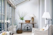 a chic vintage sunroom space with a neutral chair, a wooden table and some elegant lamps
