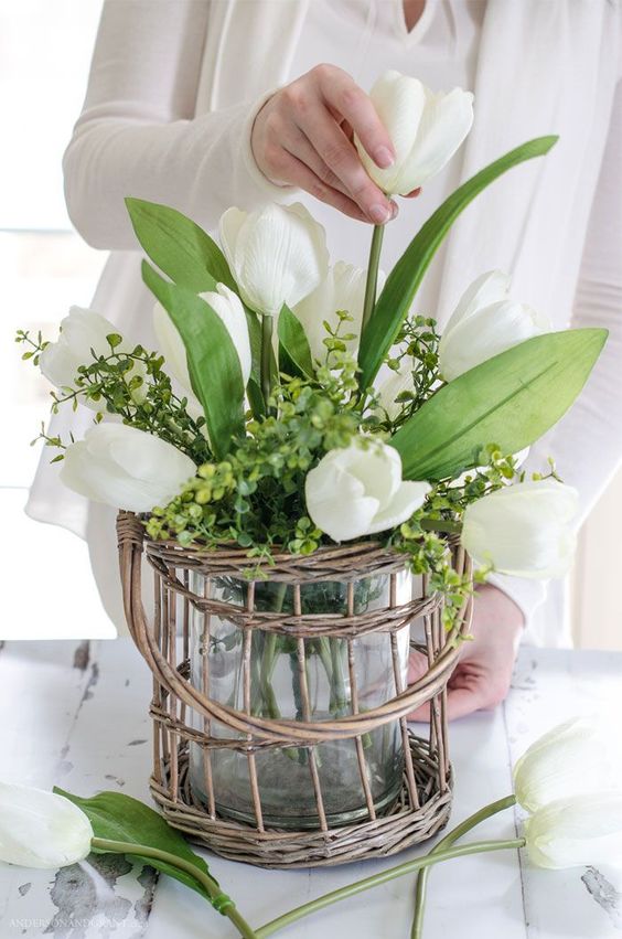 a clear vase with green hydrangeas and white tulips placed in a wicker holder is a lovely spring decoration in rustic style