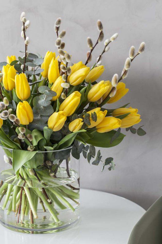 a clear vase with yellow tulips and willow plus a bit of eucalyptus is a lovely and bold spring flower arrangement
