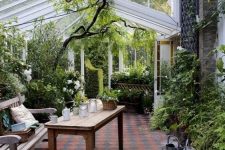 a conservatory with lots of greenery and blooms, wooden furniture and candle lanterns