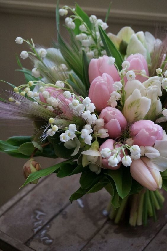 a pretty floral arrangemnt with pink and white tulips, lily of the valley, some grass and leaves is amazing for spring