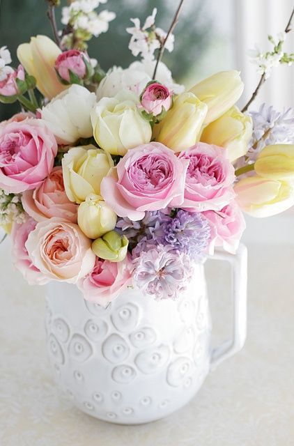 a pretty jug with yellow tulips, pink and peachy peony roses, cherry blossom and purple blooms is a bright spring arrangement