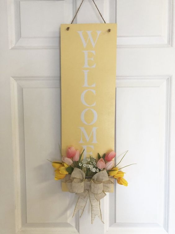 a simple yellow sign with pink and yellow blooms, greenery and a burlap bow will substitute a usual door wreath