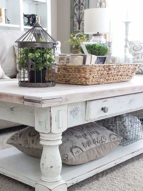 a white shabby chic coffee table with a wire basket and a pillw that are stored under the tabletop