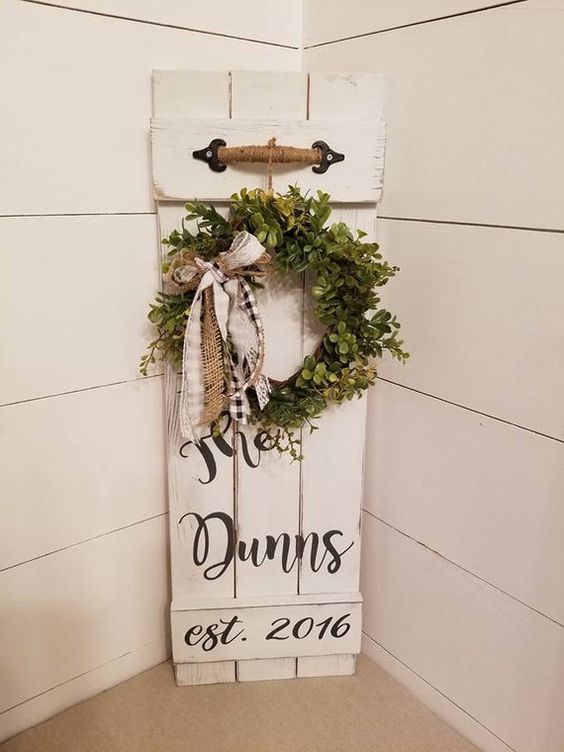 a white sign with a greenery wreath, burlap and plaid bows, a twine handle is a chic idea for a rustic space