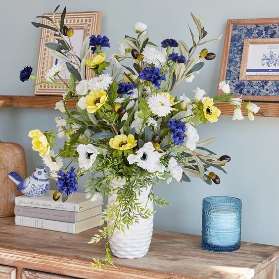 a white textural vase with white, purple and yellow blooms and olive branches with olives is a non-typical idea