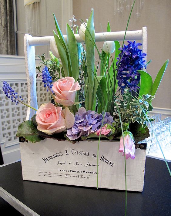 a white toolbox with purple hyacinths, pink roses, white tulips and some greenery is a beautiful and chic decoration