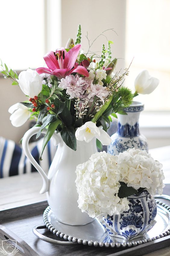 a white vase with pink, blush and white blooms, greenery and twigs of various kinds for a spring rustic space