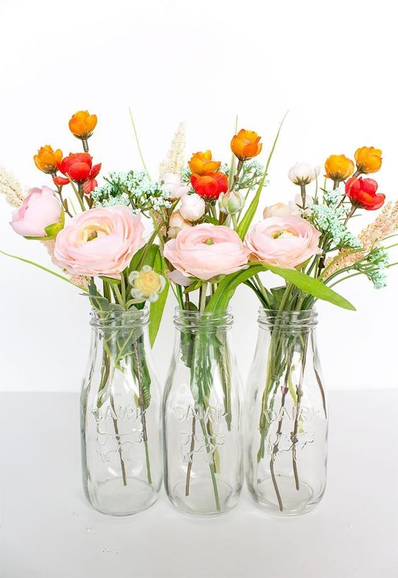 bottles with pink ranunculus and smaller red and orcher blooms plus grasses are fresh spring decorations