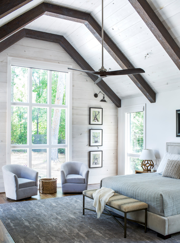 a large airy farmhouse bedroom done with white walls, dark stained ceiling beams and comfy furniture  (Sheehan Built Homes)