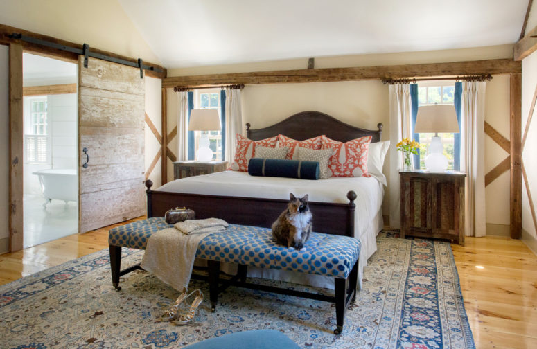 a farmhouse bedroom with much weathered and aged wood, traditional textiles and a sliding barn door  (Cummings Architects)