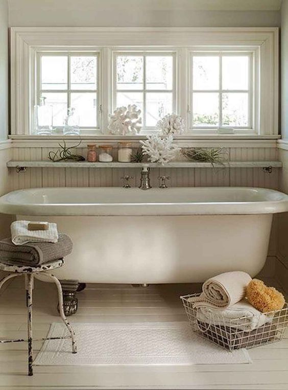 a beach bathroom with beadboard, a vintage clawfoot tub, a wire basket and a metal stool