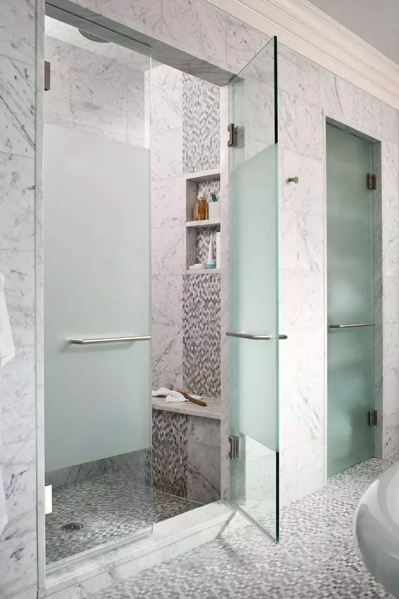 A built in shower space with grey and white marble tiles, forsted glass doors and handles and built in lights