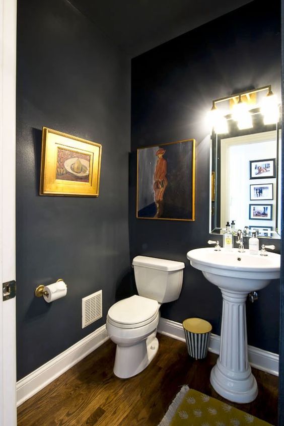 a chic and refined powder room with chalkboard walls, a pedestal sink and a toilet, a mirror with lights and some vintage artwork