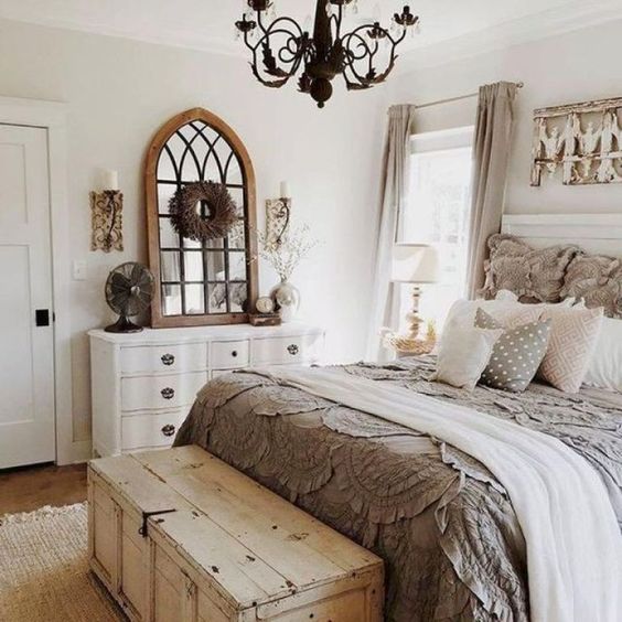 a chic farmhouse bedroom in neutrals, with vintage furniture, a chest for storage and a metal chandelier