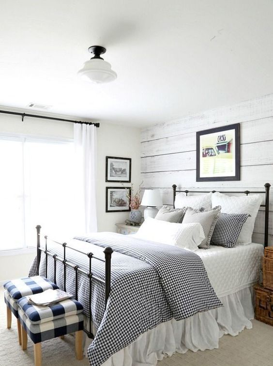 a classic farmhouse bedroom with whitewashed wooden walls, checked and gingham prints and a metal bed