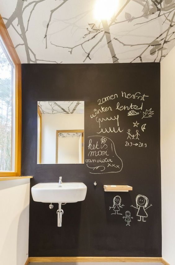 A cool powder room with a black chalkboard accent wall, a wall mounted sink, a small shelf and a mirror