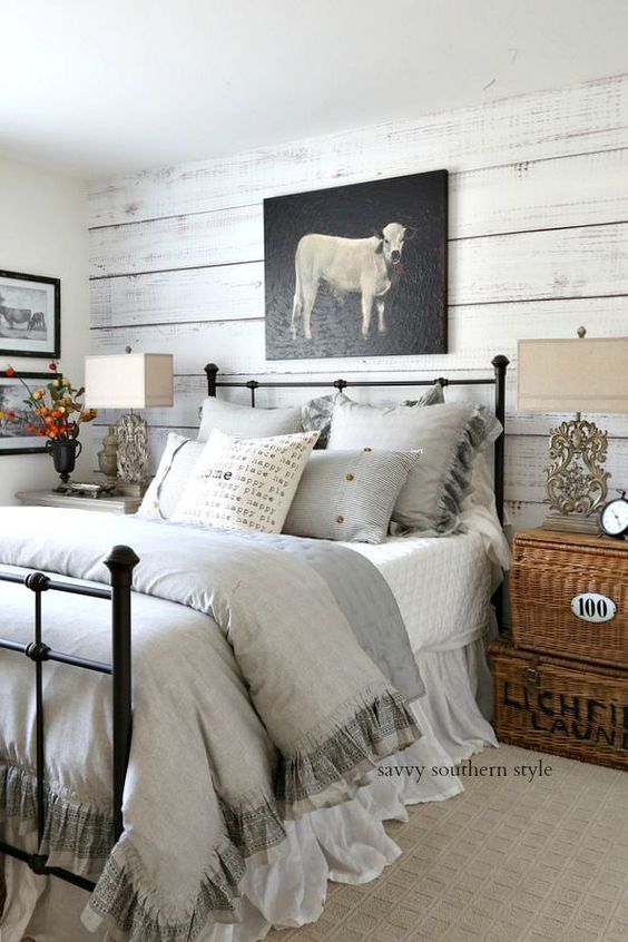 a farmhouse bedroom with whitewashed walls, neutral textiles, basket boxes and a cow artwork