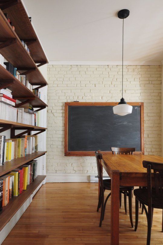 a farmhouse studying and working space with a brick wall, a stained table and chairs, a framed chalkboard and a floating bookcase