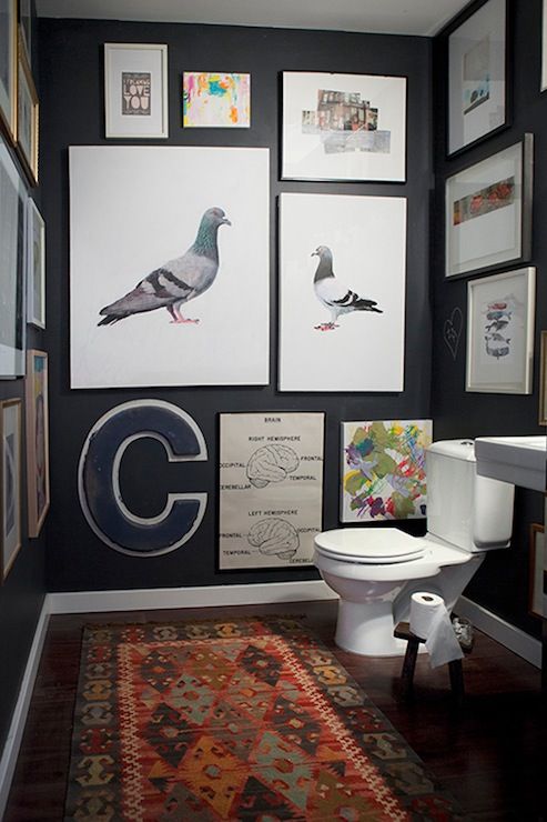 A modern powder room with chalkboard walls, a lot of artwork covering the walls, a wall mounted sink and a printed rug
