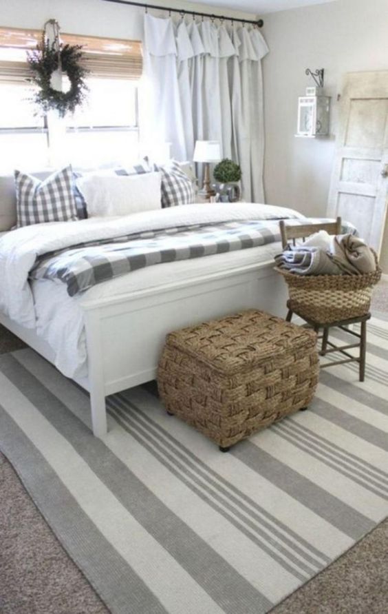a neutral farmhouse bedroom with checked and striped textiles, a wicker chest and greenery