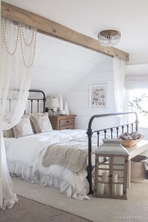 a neutral farmhouse space with a wooden beam with beads and curtains, a large candle lantern and neutral textiles