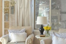 a neutral farmhouse sunroom with elegant vintage furniture, a lamp, blooms and a calligraphy sign over the chairs