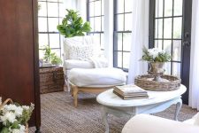 a refined farmhouse sunroom with elegant neutral furniture, baskets and chests, potted greenery and blooms and shades