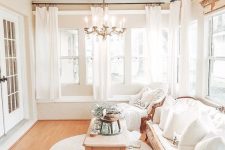 a refined neutral French farmhouse sunroom with elegant furniture, a wooden table, greenery, a vintage chandelier and wooden beams on the ceiling