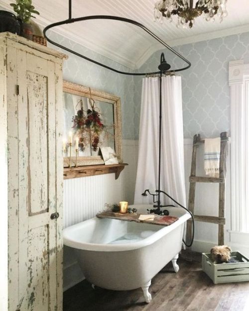 a shabby chic farmhouse bathroom with grey printed wallpaper, a white clawfoot tub, a shabby chic storage unit, a mirror in a wooden frame