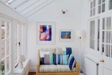 a simple and modern sunroom with a small wicker sofa with colorful pillows, artworks and a coffee table