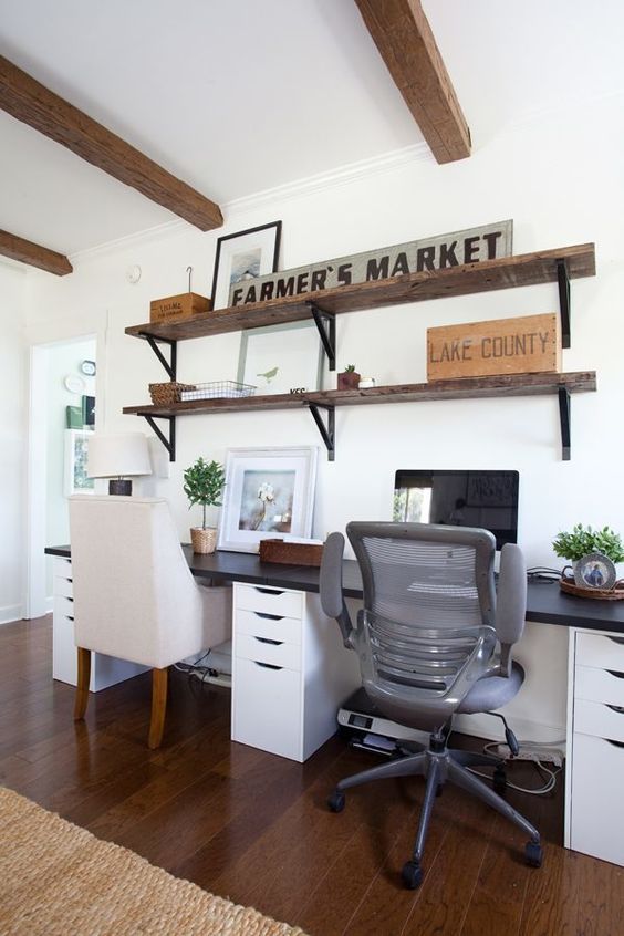 a simple farmhouse home office with industrial shelves, a shared desk, modern chairs and some potted greenery