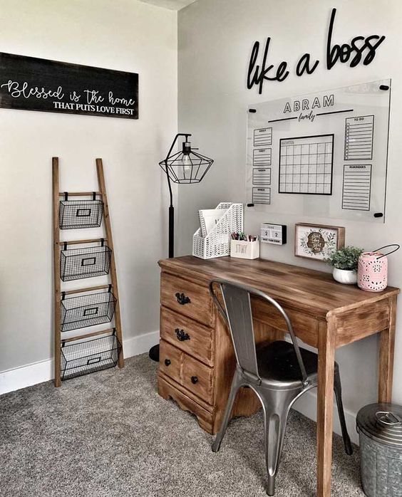 a small and cozy farmhouse home office with a wooden desk, a metal chair, a ladder and wire basket storage unit and an acrylic board