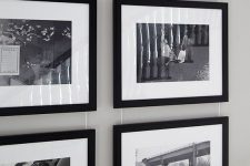 a stylish gallery wall with photos in black frames hanging on wire from above is a chic decor idea