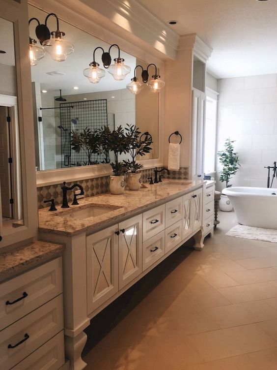 a vintage farmhouse bathroom with a large creamy vanity, vintage lamps and storage units plus a modern tub