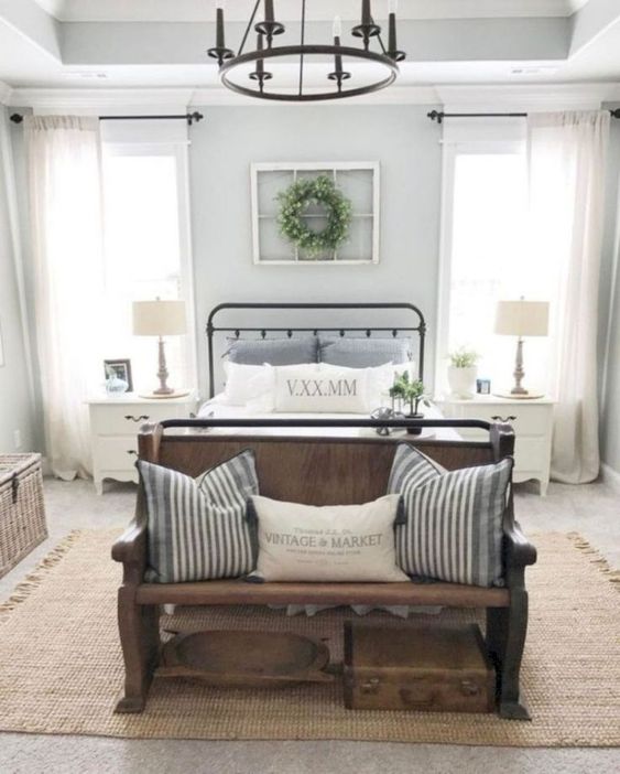 a vintage farmhouse bedroom with a metal chandelier, a wooden bench and striped textiles