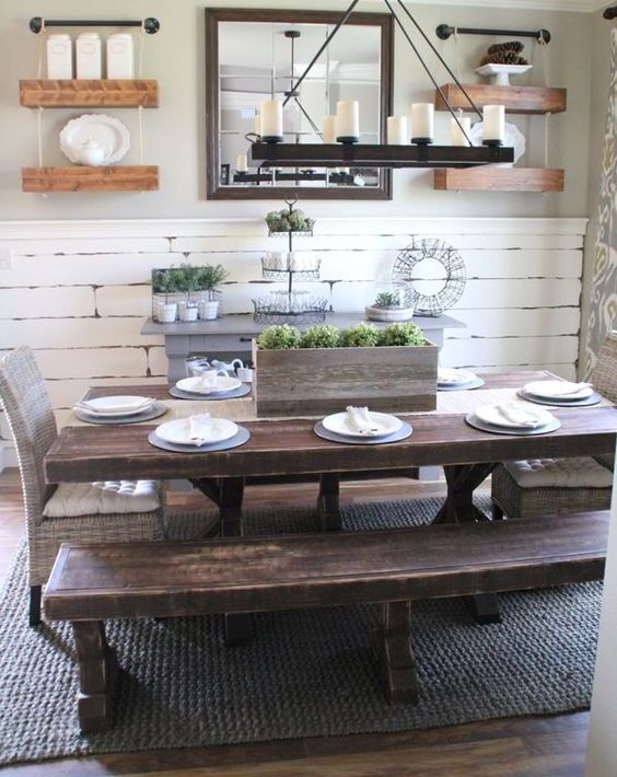 a vintage farmhouse dining area with a whitewashed wall, shelves, dark stained wooden dining set and a wooden chandelier