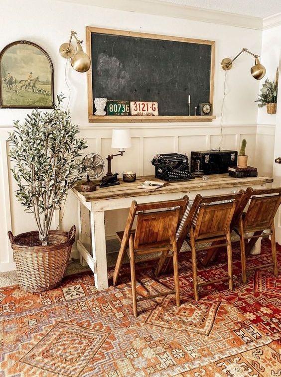 a vintage farmhouse home office with a large desk, several chairs, a chalkboard, brass lamps and potted plants