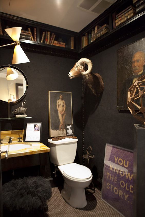 a vintage powder room with black chalkboard walls, bookshelves, a vanity with a snk and some bold decor