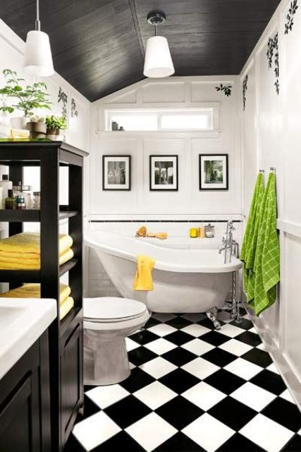 a bold vintage bathroom with a black slanted ceiling, a black and white tile floor, black cabinets and a clawfoot tub plus bold textiles