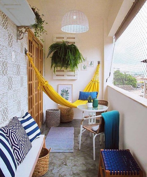 a bright and cheerful summer balcony in yellow and blue, with printed and just bright textiles, a yellow hammock and some greenery