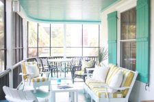 a bright mint blue sunroom with white wooden furniture, striped upholstery and a cozy dining space