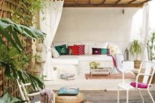 a bright summer terrace with a built-in bench, with bright pillows, rugs, wicker ottoman, potted greenery