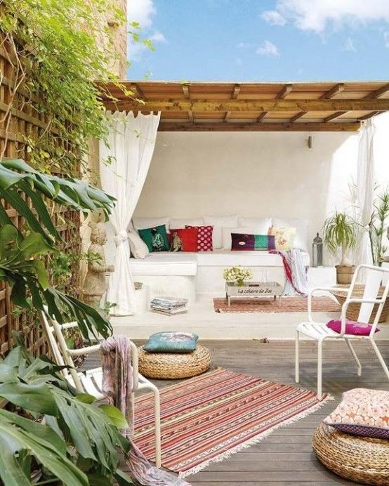A bright summer terrace with a built in bench, with bright pillows, rugs, wicker ottoman, potted greenery