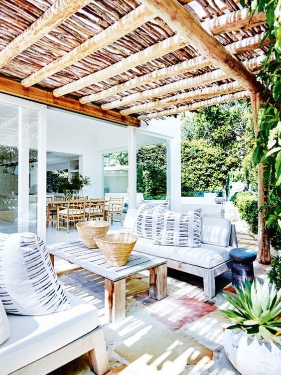 A bright summer terrace with wooden furniture, watercolor rugs and striped pillows feels very island like
