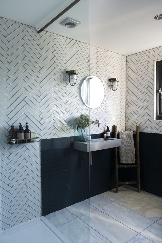A catchy and chic bathroom with white herringbone tiles, a black backsplash, a concrete wall mounted sink and vintage lamps