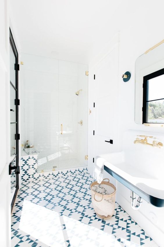 A catchy bathroom with a blue and white tile floor, a wall mounted sink, black and gold fixtures and touches