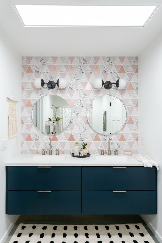 a catchy bathroom with a geo tile wall, a navy built-in vanity and round mirrors plus vintage wall sconces